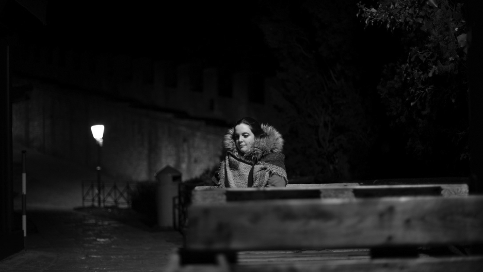 Una donna sola che pensa alla luce di un lampione seduta su una panchina.