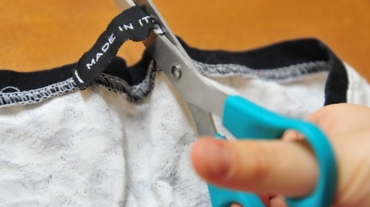 Una mano di un bambino che con una forbice toglie l'etichetta alla maglia
