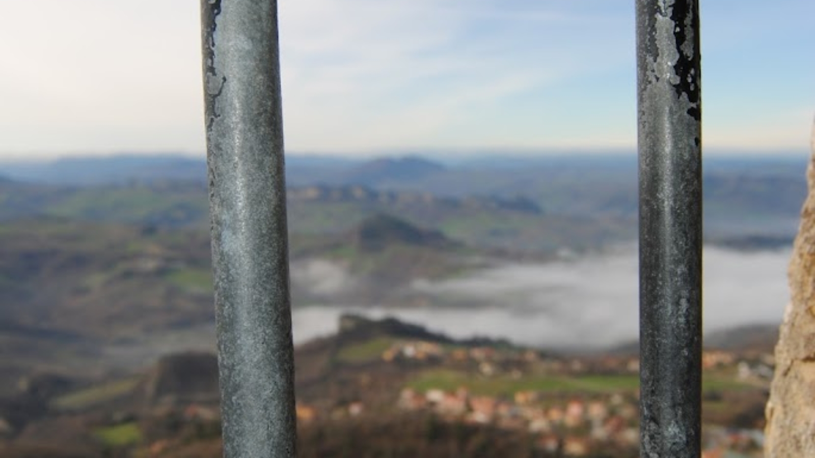 Una grata di una finestra si affaccia a un paesaggio fatto di case e colline