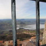 Una grata di una finestra si affaccia a un paesaggio fatto di case e colline