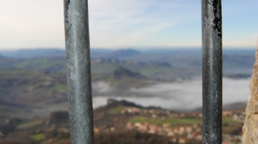 Una grata di una finestra si affaccia a un paesaggio fatto di case e colline