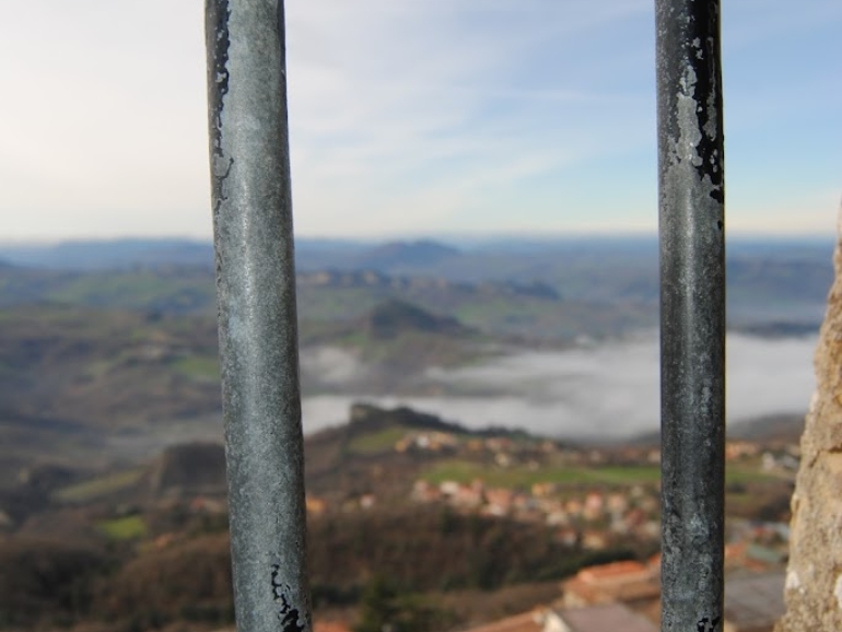 Una grata di una finestra si affaccia a un paesaggio fatto di case e colline