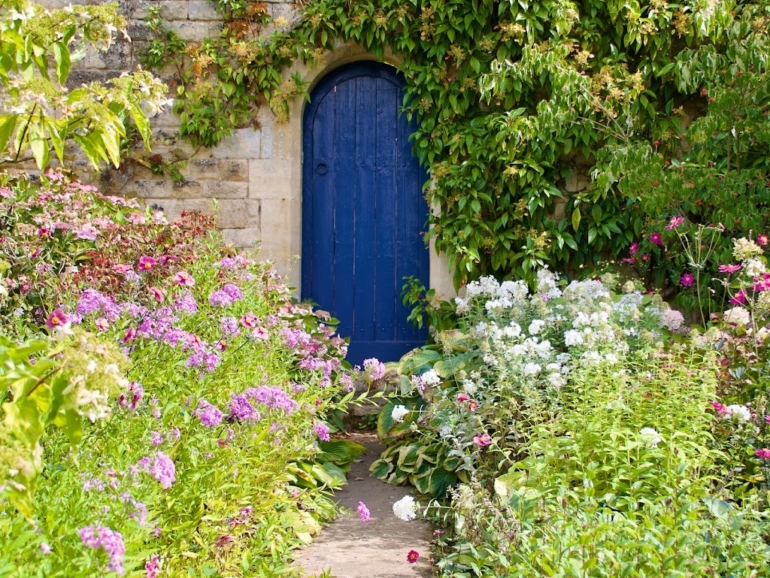 Una porta blu attraverso un giardino fiorito
