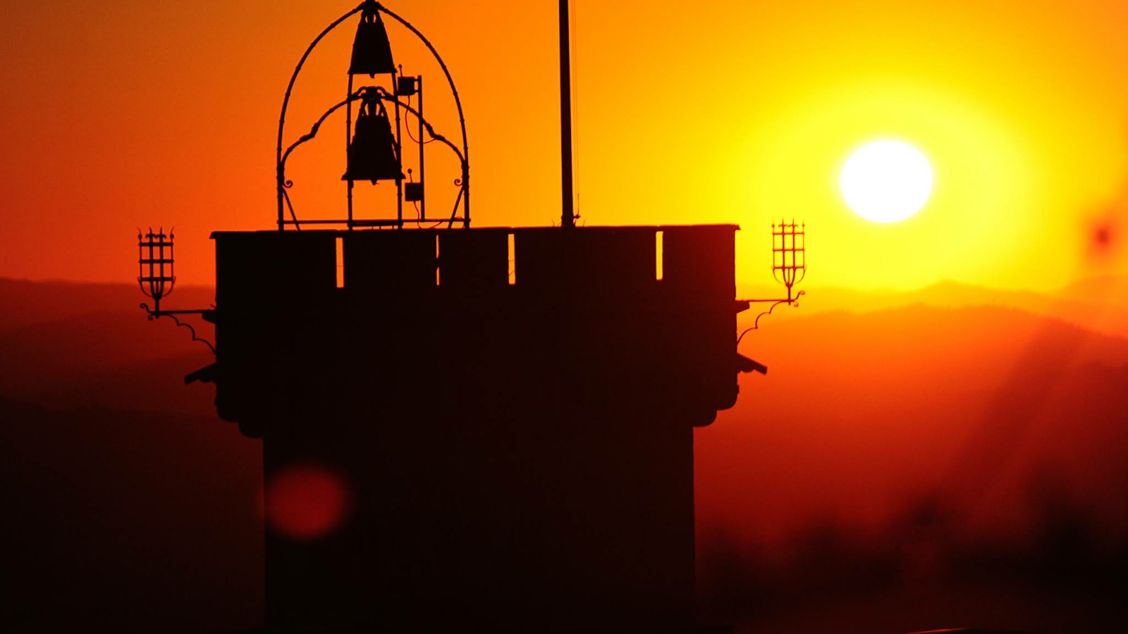 Una torre con una campana sopra, in contrasto con un splendido tramonto arancione