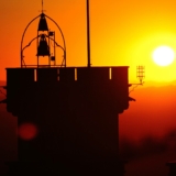 Una torre con una campana sopra, in contrasto con un splendido tramonto arancione